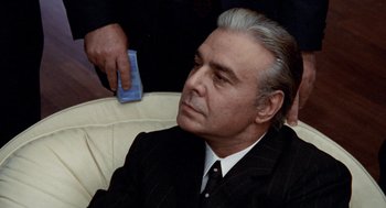 Movie still from “Investigation of a Citizen Above Suspicion” (1970), directed by Elio Petri – An older man in a suit and tie holding something; Close Up shot, Over the shoulder angle