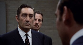 Movie still from “Investigation of a Citizen Above Suspicion” (1970), directed by Elio Petri – Two men in suits looking at each other in front of a brick wall; Close Up shot, Over the shoulder angle