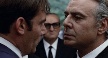 Movie still from “Investigation of a Citizen Above Suspicion” (1970), directed by Elio Petri – Two men in business suits face each other in front of another man in a suit and tie; Close Up shot, Over the shoulder angle