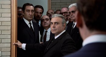 Movie still from “Investigation of a Citizen Above Suspicion” (1970), directed by Elio Petri – A group of men standing around a man in a black suit; Medium shot, Over the shoulder angle