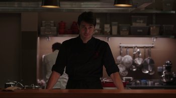 Movie still from “Emily in Paris” (2020), created by Darren Star – A man standing behind a counter in a kitchen; Medium shot, Over the shoulder angle