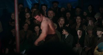 Movie still from “Invincible” (2001), directed by Werner Herzog – A crowd of people are watching a shirtless man; Medium shot, Over the shoulder angle