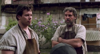 Movie still from “Invincible” (2001), directed by Werner Herzog – A man and a man in an apron standing next to each other in front of flowers; Medium shot, Over the shoulder angle