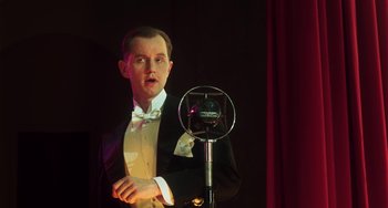 Movie still from “Invincible” (2001), directed by Werner Herzog – A man in a tuxedo standing in front of a microphone; Close Up shot, Low angle
