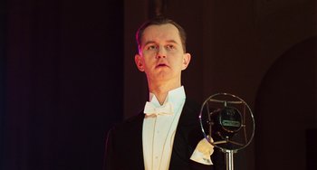 Movie still from “Invincible” (2001), directed by Werner Herzog – A man in a tuxedo standing in front of a microphone; Close Up shot, Low angle