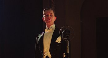 Movie still from “Invincible” (2001), directed by Werner Herzog – A man in a tuxedo standing in front of a microphone; Medium shot, Low angle
