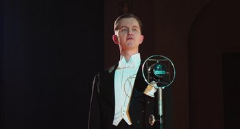 Movie still from “Invincible” (2001), directed by Werner Herzog – A man in a tuxedo standing in front of a microphone; Medium shot, Low angle