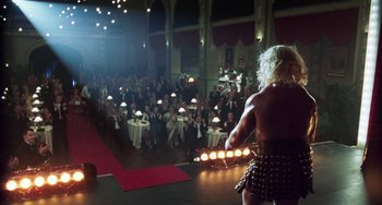 Movie still from “Invincible” (2001), directed by Werner Herzog – A crowd of people sitting and standing in a room; Wide shot, Over the shoulder angle
