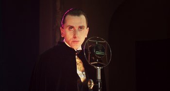 Movie still from “Invincible” (2001), directed by Werner Herzog – A man in a suit and tie standing in front of a microphone; Close Up shot, Low angle