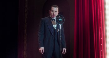 Movie still from “Invincible” (2001), directed by Werner Herzog – A man standing in front of a microphone in front of a red curtain; Medium shot, Low angle