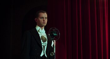 Movie still from “Invincible” (2001), directed by Werner Herzog – A man standing in front of a microphone on a stage; Medium shot, Low angle