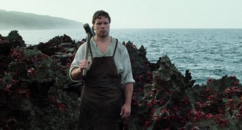Movie still from “Invincible” (2001), directed by Werner Herzog – A man holding an axe standing on a rocky shore; Medium shot, Low angle