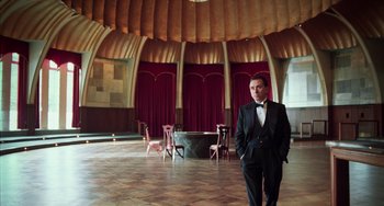 Movie still from “Invincible” (2001), directed by Werner Herzog – A man in a suit and bow tie standing in front of chairs; Wide shot, Low angle