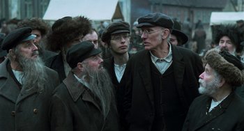 Movie still from “Invincible” (2001), directed by Werner Herzog – A group of men standing next to each other wearing hats; Medium shot, Over the shoulder angle