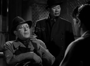 Movie still from “Invisible Agent” (1942), directed by Edwin L. Marin – A group of men standing next to each other in a room; Medium shot, Over the shoulder angle