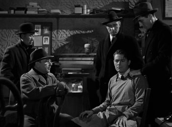 Movie still from “Invisible Agent” (1942), directed by Edwin L. Marin – A black and white photo of a group of men in a room; Medium shot, Over the shoulder angle