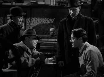 Movie still from “Invisible Agent” (1942), directed by Edwin L. Marin – A black and white photo of a group of men talking to each other; Medium shot, Over the shoulder angle