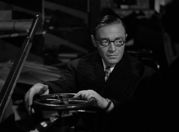 Movie still from “Invisible Agent” (1942), directed by Edwin L. Marin – A black and white photo of a man holding a steering wheel; Close Up shot, High angle