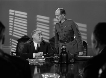Movie still from “Invisible Agent” (1942), directed by Edwin L. Marin – Two men are sitting at a table in a room; Medium shot, Over the shoulder angle