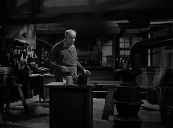 Movie still from “Invisible Agent” (1942), directed by Edwin L. Marin – An old man standing in front of a table in a room; Medium shot, High angle