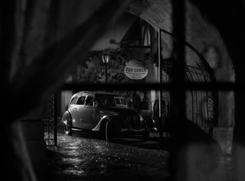 Movie still from “Invisible Agent” (1942), directed by Edwin L. Marin – An old car parked in front of a building; Wide shot, High angle