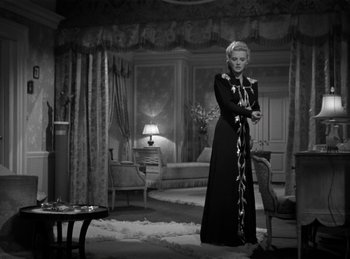 Movie still from “Invisible Agent” (1942), directed by Edwin L. Marin – A woman in a long black dress standing in a living room; Medium shot, Low angle