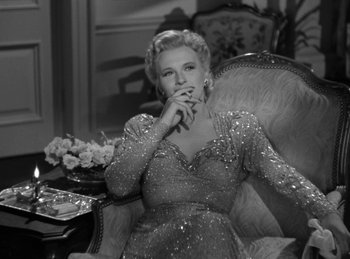 Movie still from “Invisible Agent” (1942), directed by Edwin L. Marin – An old photo of a woman sitting in a chair smoking a cigarette; Medium shot, Low angle