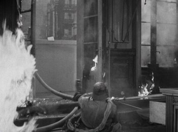 Movie still from “Invisible Agent” (1942), directed by Edwin L. Marin – A man holding a fire hydrant while standing in front of a building; Wide shot, High angle