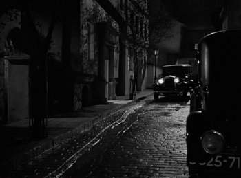 Movie still from “Invisible Agent” (1942), directed by Edwin L. Marin – An old car is parked on the side of the street; Wide shot, High angle