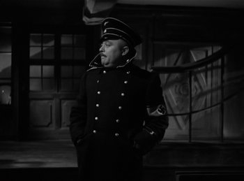 Movie still from “Invisible Agent” (1942), directed by Edwin L. Marin – A man in a military uniform standing in front of a building; Medium shot, Low angle