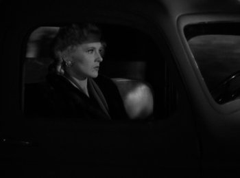 Movie still from “Invisible Agent” (1942), directed by Edwin L. Marin – A black and white photo of a woman sitting in the back of a car; Close Up shot, High angle
