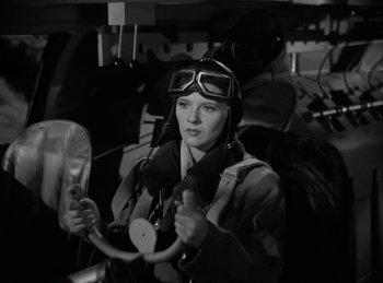 Movie still from “Invisible Agent” (1942), directed by Edwin L. Marin – A woman in a pilot's uniform is holding a steering wheel; Medium shot, Low angle