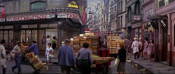 Movie still from “Irma la Douce” (1963), directed by Billy Wilder – A group of people walking down a street near boxes of fruit; Wide shot, High angle