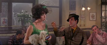 Movie still from “Irma la Douce” (1963), directed by Billy Wilder – A man and a woman are smoking a cigarette and holding a dog; Medium shot, Low angle