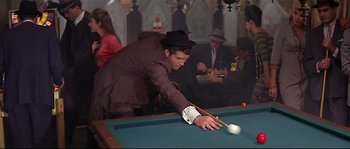 Movie still from “Irma la Douce” (1963), directed by Billy Wilder – A man in a suit and hat playing a game of billiards; Medium shot, Over the shoulder angle