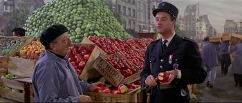 Movie still from “Irma la Douce” (1963), directed by Billy Wilder – A man in a police uniform standing in front of boxes of apples; Medium shot, Over the shoulder angle