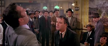 Movie still from “Irma la Douce” (1963), directed by Billy Wilder – A group of men in suits and hats standing in a room; Medium shot, Over the shoulder angle