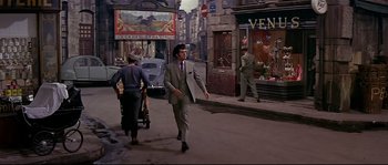 Movie still from “Irma la Douce” (1963), directed by Billy Wilder – A man walking down a street while a woman pushes a stroller; Wide shot, High angle