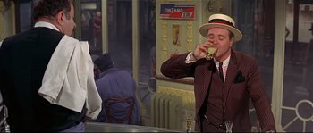 Movie still from “Irma la Douce” (1963), directed by Billy Wilder – A man wearing a hat and eating a piece of food; Medium shot, Over the shoulder angle