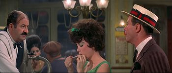 Movie still from “Irma la Douce” (1963), directed by Billy Wilder – A woman in a green dress putting lipstick on her lips; Medium shot, Low angle