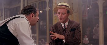 Movie still from “Irma la Douce” (1963), directed by Billy Wilder – A man wearing a suit and hat talking to another man; Medium shot, Over the shoulder angle