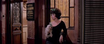 Movie still from “Irma la Douce” (1963), directed by Billy Wilder – A woman holding a small white dog in her arms; Medium shot, Low angle
