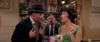 Movie still from “Irma la Douce” (1963), directed by Billy Wilder – A group of people sitting around a table with a dog; Medium shot, Over the shoulder angle