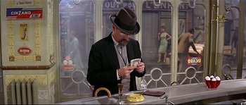 Movie still from “Irma la Douce” (1963), directed by Billy Wilder – A man in a suit and a hat looking at his cell phone; Medium shot, Low angle