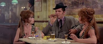 Movie still from “Irma la Douce” (1963), directed by Billy Wilder – A man in a hat is eating a piece of pizza; Medium shot, Over the shoulder angle