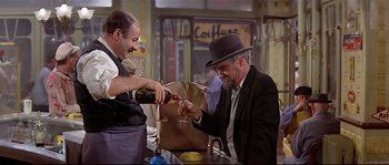 Movie still from “Irma la Douce” (1963), directed by Billy Wilder – A man in a suit and a hat is pouring a glass of wine; Medium shot, High angle