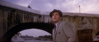 Movie still from “Irma la Douce” (1963), directed by Billy Wilder – A man wearing a suit and a hat looking up at a bridge; Medium shot, Low angle
