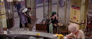 Movie still from “Irma la Douce” (1963), directed by Billy Wilder – A woman sitting at a table eating a sandwich; Wide shot, High angle