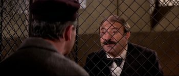 Movie still from “Irma la Douce” (1963), directed by Billy Wilder – A man in a suit and a hat talking to another man in front of a fence; Medium shot, Over the shoulder angle