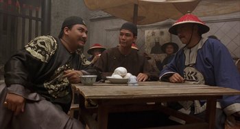 Movie still from “Iron Monkey” (1993), directed by Woo-Ping Yuen – A group of men sitting at a table under an umbrella; Medium shot, Over the shoulder angle